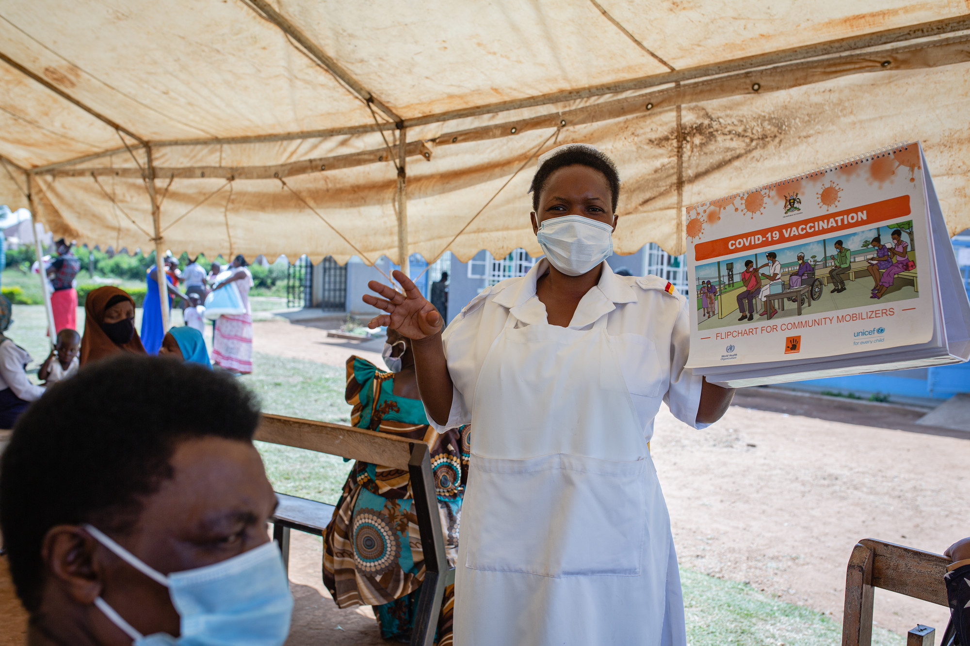 A health worker talks to waiting clients about COVID-19 vaccinations at Nakaloke Health Center III in Mbale, Uganda. Photo by Esther Ruth Mbabazi for IntraHealth International. 